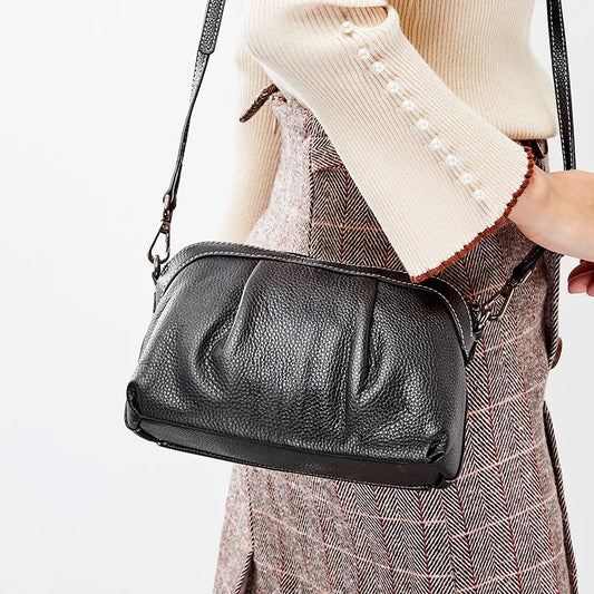 Black leather handbag being carried by a person wearing a beige sweater and plaid skirt.